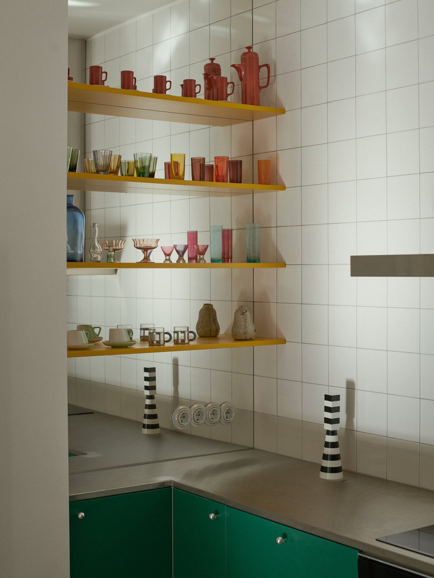 E6 apartment: yellow shelves with colourful ceramics above green cabinets